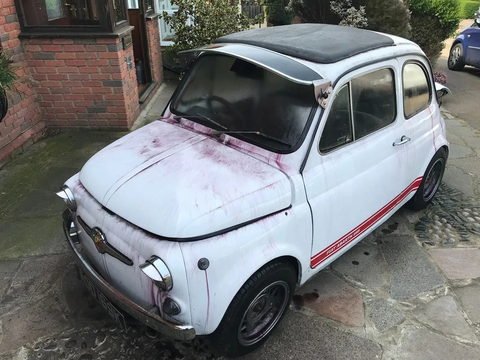 Restored vintage Fiat parked outside a brick home