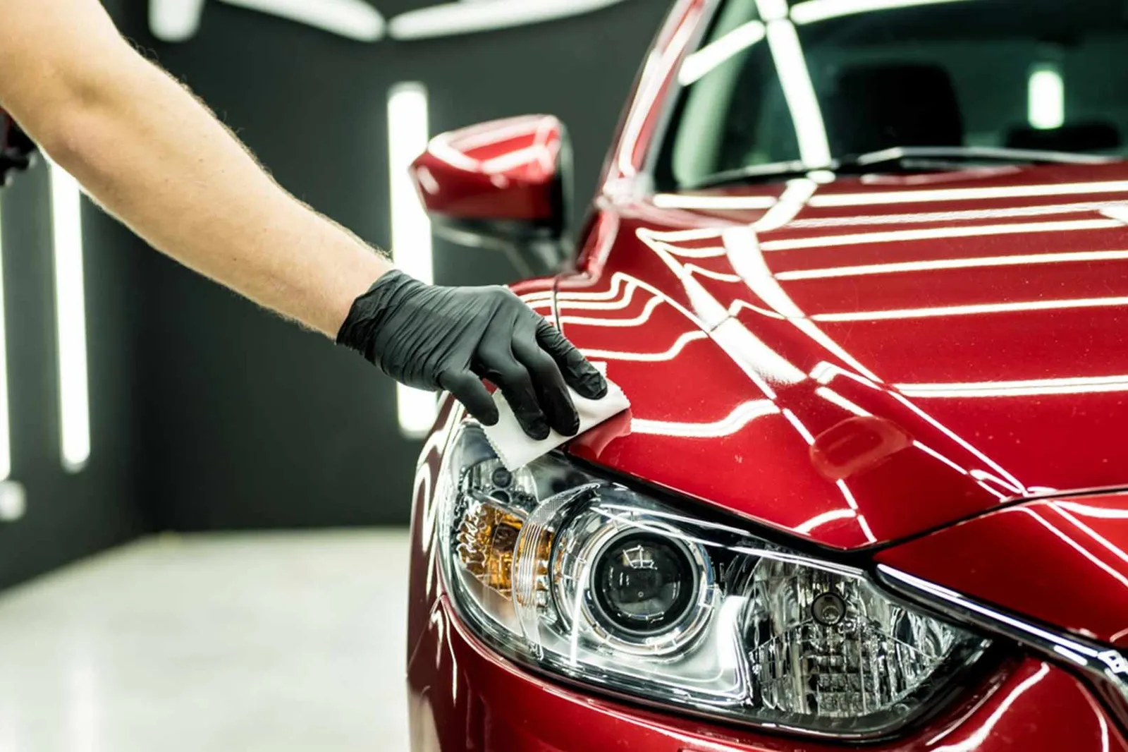 Technician machine polishing the headlight area of a red car
